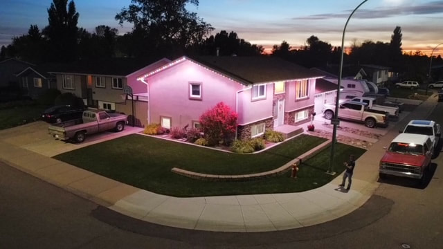 A Lethbridge home at dusk, its rooflines washed in magenta by a Gemstone permanent lighting install, photographed from the air.